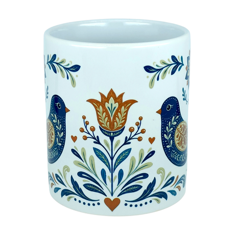 Introducing the Mug: Nordic Folk Art Birds Ceramic Mug (11 oz Capacity) by Nordic Wholesale—an elegant white ceramic mug adorned with a symmetrical folk art motif featuring two blue birds, a central orange and yellow flower, leafy accents, and delicate orange hearts. Ideal for anyone who loves the timeless appeal of Scandinavian design.