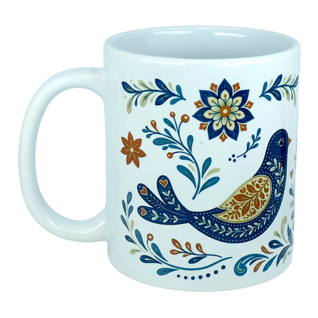 The Nordic Wholesale Mug: Nordic Folk Art Birds Ceramic Mug (11 oz Capacity) features a white ceramic design decorated with a Scandinavian-inspired blue and gold folk-art bird, surrounded by intricate blue, gold, and orange floral and leafy patterns.