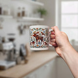 A hand holds the Swedish Gift Store's Mug: Nordic Forest Kurbits Dala Moose Wraparound Ceramic Mug (11 oz), featuring a folk-art moose and floral designs; a blurred kitchen appears in the background.