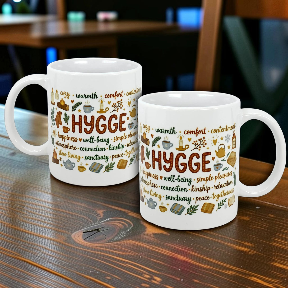 Two Nordic Hygge Comfort Typography Ceramic Mugs (11 oz) by Swedish Gift Store sit on a wooden table, each adorned with cozy-themed words and illustrations for a warm Scandinavian vibe.