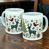 Two Nordic Wholesale "Nordic Forest Reindeer & Christmas Tree" ceramic mugs (11 oz), featuring festive designs with reindeer, red birds, Christmas trees, holly, and gift boxes, sit on a wooden table.