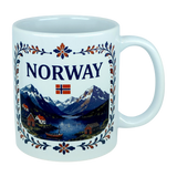 The Nordic Wholesale Mug: Norway Fjord Mountain Ceramic Mug (11 oz Capacity) features the word "NORWAY" and a Norwegian flag above a scenic illustration of mountains, water, boats, and houses, all framed by blue and orange floral patterns inspired by traditional rosemaling. This ceramic mug beautifully celebrates Norwegian heritage with its intricate design.