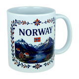 The Nordic Wholesale Mug: Norway Fjord Mountain Ceramic Mug (11 oz Capacity) features the word "NORWAY," a small Norwegian flag, and a detailed illustration of mountains, a fjord, houses, trees, and a boat. The design is framed by an elegant floral border inspired by traditional rosemaling. This charming mug beautifully celebrates Norwegian heritage with every sip.