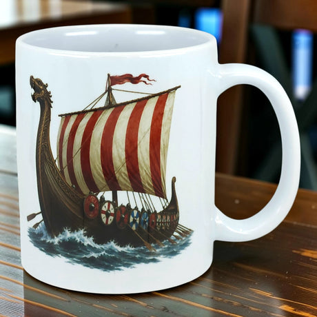 Ceramic mug featuring a Viking longship with a red and white striped sail, wooden shields along the sides, and stylized waves beneath the hull.