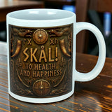 A white 11 oz "Skal To Health And Happiness" Norse ceramic mug by Nordic Wholesale, featuring decorative Viking-style artwork with axes, shields, drinking horns, classic Norse patterns, and the text “SKÅL! TO HEALTH AND HAPPINESS.”.