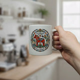 A hand holds the Swedish Gift Store’s "Sverige Dala Häst" mug—an 11 oz ceramic cup featuring a red Dala Horse with a Swedish folk art wreath—in a bright, modern kitchen.