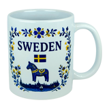 The Nordic Wholesale Mug: Sweden Dala Horse Ceramic Mug (11 oz Capacity) features blue and yellow floral designs, the word "SWEDEN," a small Swedish flag, and a traditional blue Dala horse above a silhouette of buildings—beautifully celebrating Swedish heritage in this charming Scandinavian folk mug.