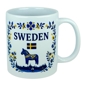 The Nordic Wholesale Mug: Sweden Dala Horse Ceramic Mug (11 oz Capacity) features blue and yellow floral designs, the word "SWEDEN," a small Swedish flag, and a traditional blue Dala horse above a silhouette of buildings—beautifully celebrating Swedish heritage in this charming Scandinavian folk mug.