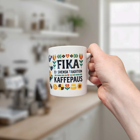 A hand holds the Nordic Wholesale Mug: Fika — "En Svensk Tradition Kaffepaus" 11 oz ceramic mug, decorated with colorful Scandinavian patterns—an ideal Swedish tradition gift for any modern kitchen.