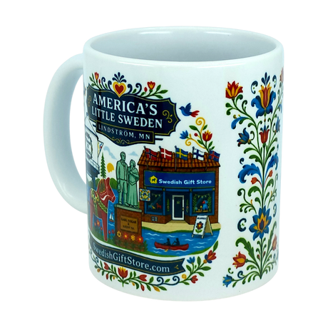 Introducing the Mug: Swedish Gift Store America's Little Sweden Ceramic Mug (11 oz) by Nordic Wholesale. This white ceramic mug showcases vibrant Swedish folk art, a storefront with the “Swedish Gift Store” sign, and a statue, along with text that reads “America’s Little Sweden, Lindström, MN.” The handle and right side are adorned with charming floral patterns and a cheerful Dala horse design for an authentic Nordic touch.