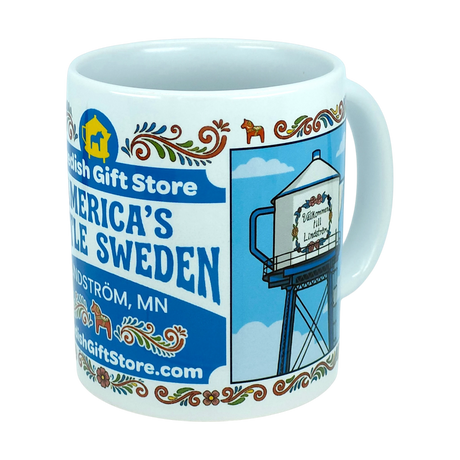 Introducing the Mug: Swedish Gift Store America's Little Sweden Wraparound Ceramic Mug (11 oz) by Nordic Wholesale—a white ceramic mug adorned with Swedish folk patterns, "Swedish Gift Store" text, and a wraparound illustration of a water tower labeled "America’s Little Sweden," celebrating the heritage of Lindström, MN—making it the perfect mug for Swedish-American pride.