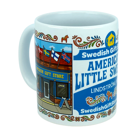 Enjoy your favorite beverage with the Mug: Swedish Gift Store America's Little Sweden Wraparound Ceramic Mug (11 oz) by Nordic Wholesale. This white ceramic mug features a vibrant storefront labeled "Swedish Gift Store," highlighted by Scandinavian flags, decorative Swedish folk art, and a delightful Dala horse design. The text reads "America's Little Sweden" and "Lindström," making it the perfect piece to celebrate your Swedish-American heritage.