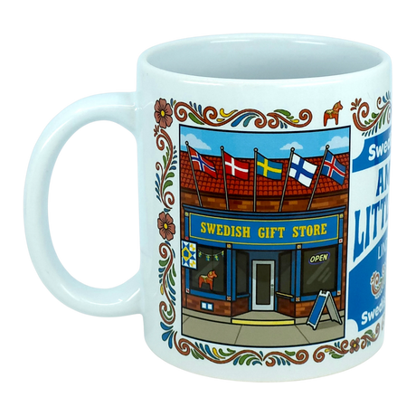 The Nordic Wholesale "Mug: Swedish Gift Store America's Little Sweden Wraparound Ceramic Mug" (11 oz) is a white ceramic mug adorned with an illustration of a Swedish gift store, complete with Scandinavian flags above the entrance and floral decorative borders along the edge.