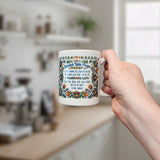 A hand holds the Nordic Wholesale Mug: Swedish Table Prayer Ceramic Kurbits Mug (11 oz Capacity) in a kitchen, with blurred shelves and appliances in the background.