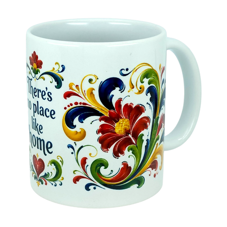 Introducing the Mug: There's No Place Like Home Rosemaling Ceramic Mug (11 oz) by Nordic Wholesale—a white ceramic coffee mug adorned with vibrant red, yellow, green, and blue floral motifs and scrolling patterns inspired by Scandinavian folk art. Part of the design includes the phrase "There's no place like home," while the handle remains plain.