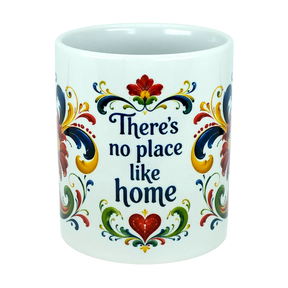 The Nordic Wholesale "There's No Place Like Home" Rosemaling Ceramic Mug (11 oz) is a white ceramic coffee mug featuring vibrant Scandinavian folk art-inspired floral designs and "There's no place like home" written in blue on the front.