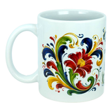 The Nordic Wholesale "There's No Place Like Home" Rosemaling Ceramic Mug (11 oz) is a white mug adorned with a vibrant Scandinavian folk art-inspired floral and leaf design in red, yellow, green, and blue, featuring swirling patterns and a prominent central flower.
