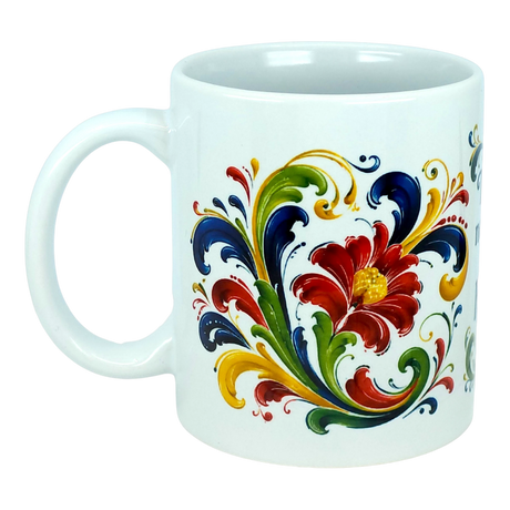 The Nordic Wholesale "There's No Place Like Home" Rosemaling Ceramic Mug (11 oz) is a white mug adorned with a vibrant Scandinavian folk art-inspired floral and leaf design in red, yellow, green, and blue, featuring swirling patterns and a prominent central flower.