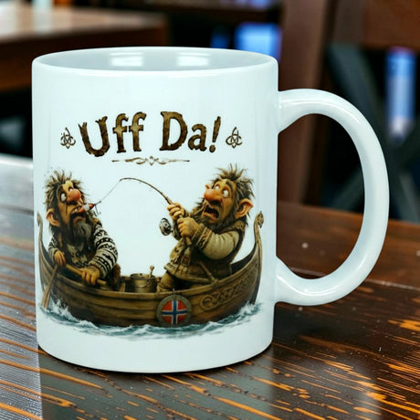 The Nordic Wholesale Mug: Uff Da Fishing Trolls Ceramic Mug (11 oz Capacity) showcases two cartoon trolls fishing from a wooden boat, with "Uff Da!" displayed above them and a small Norwegian flag on the boat. This Scandinavian humor mug is pictured against a softly blurred indoor background.