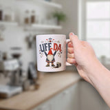 A hand holds a white mug with a tomte gnome illustration, a spilled drink graphic, and the text Uff Da.