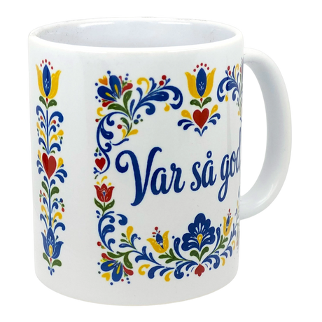 White mug featuring colorful Swedish folk art floral motifs and blue text reading “Var så god” on the side.