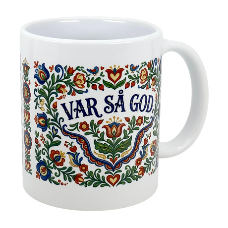 The Swedish Gift Store’s 11 oz ceramic mug features colorful kurbits folk art and the Swedish phrase "VAR SÅ GOD" in bold blue letters at the center.