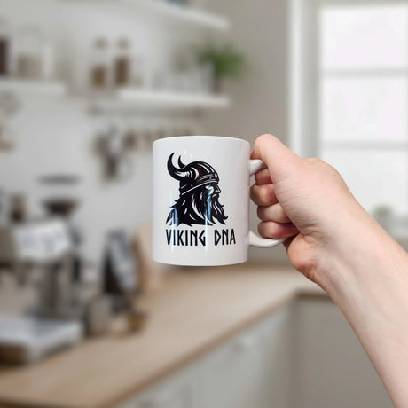 A hand holds the Nordic Wholesale Mug: Viking DNA White Ceramic Mug (11 oz), featuring a helmeted warrior and VIKING DNA text, celebrating Norse heritage in a modern kitchen.