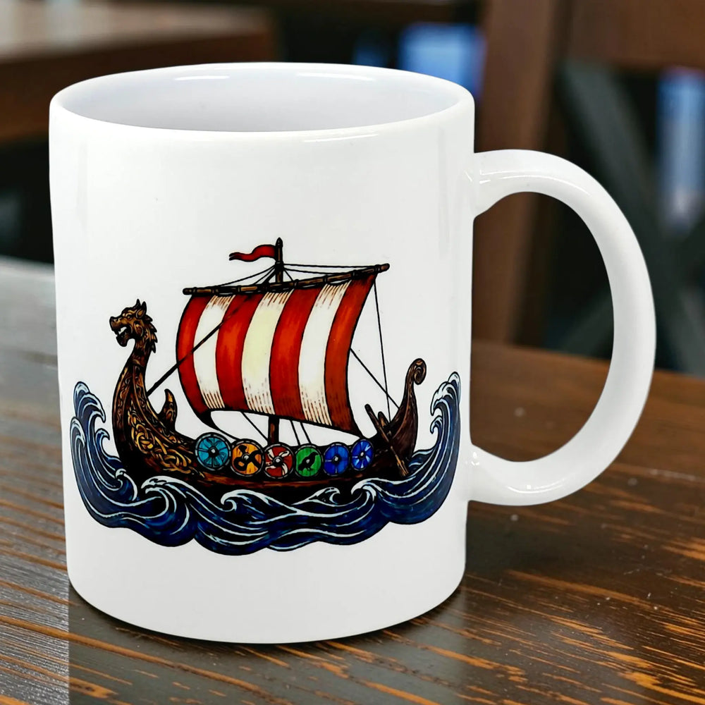 Mug featuring a Viking longship with a dragon-shaped prow, red-and-white striped sail, colorful shields along the side, and blue waves beneath the ship.