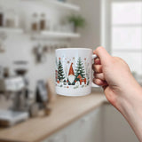 A hand holds the Nordic Wholesale Mug: Winter Tomte and Dala Horse Ceramic Mug (11 oz), featuring festive Scandinavian gnomes, Dala horses, and wintry designs in a bright kitchen background.