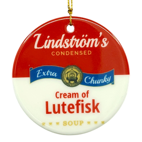 Round ornament styled like a soup can label, text reads Lindströms Condensed Extra Chunky Cream of Lutefisk Soup, gold hanging string attached.
