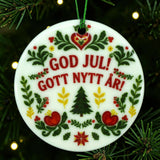 Round white ceramic ornament with a green and red folk-art Christmas tree pattern and the Swedish text GOD JUL! GOTT NYTT ÅR!.