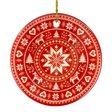 Round red Nordic ornament featuring white snowflake, reindeer, and tree patterns, hanging from a gold string.