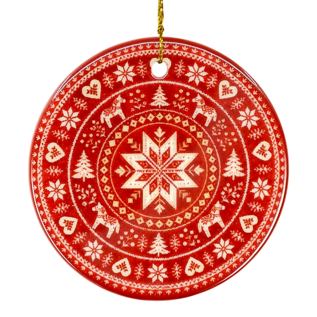 Round red Nordic ornament featuring white snowflake, reindeer, and tree patterns, hanging from a gold string.