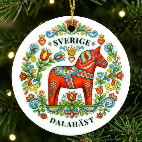Round ornament with a red Dala horse decorated in colorful floral patterns and the words SVERIGE DALAHÄST, shown hanging on a Christmas tree branch.