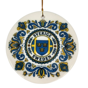 The Ornament: Sverige Sweden Triple Crown Ceramic Ornament (2.875" Diameter) by Nordic Wholesale showcases blue and yellow floral patterns surrounding a central shield with three crowns and the words "Sverige Sweden." A gold string is attached at the top, making this Swedish ceramic ornament a charming piece of Nordic holiday decor.