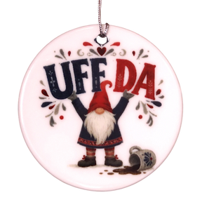 Round ceramic ornament featuring a tomte lifting the text UFF DA over his head with a spilled mug nearby.