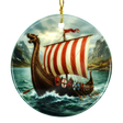 Round ceramic ornament with a Viking longship, red-and-white striped sail, ocean waves, distant mountains, and cloudy sky; hangs from a gold string.