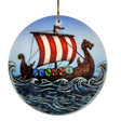 The Ornament: Viking Ship Ceramic Ornament (2.875" Diameter) by Nordic Wholesale features a round design depicting a ceramic longship with a red and white sail, dragon-shaped prow, and vibrant shields gliding through waves under a blue sky—perfect for creating striking Norse holiday décor. This ornament hangs elegantly by a gold string.