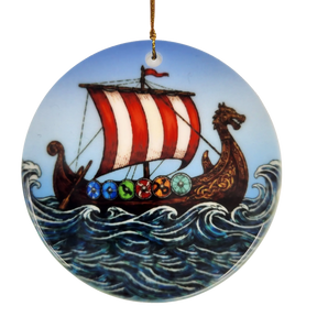 The Ornament: Viking Ship Ceramic Ornament (2.875" Diameter) by Nordic Wholesale features a round design depicting a ceramic longship with a red and white sail, dragon-shaped prow, and vibrant shields gliding through waves under a blue sky—perfect for creating striking Norse holiday décor. This ornament hangs elegantly by a gold string.