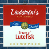 A can with a label reading Lindströms Condensed Extra Chunky Cream of Lutefisk Soup sits in front of white ceramic tile, featuring Minnesota folk art-inspired design elements.