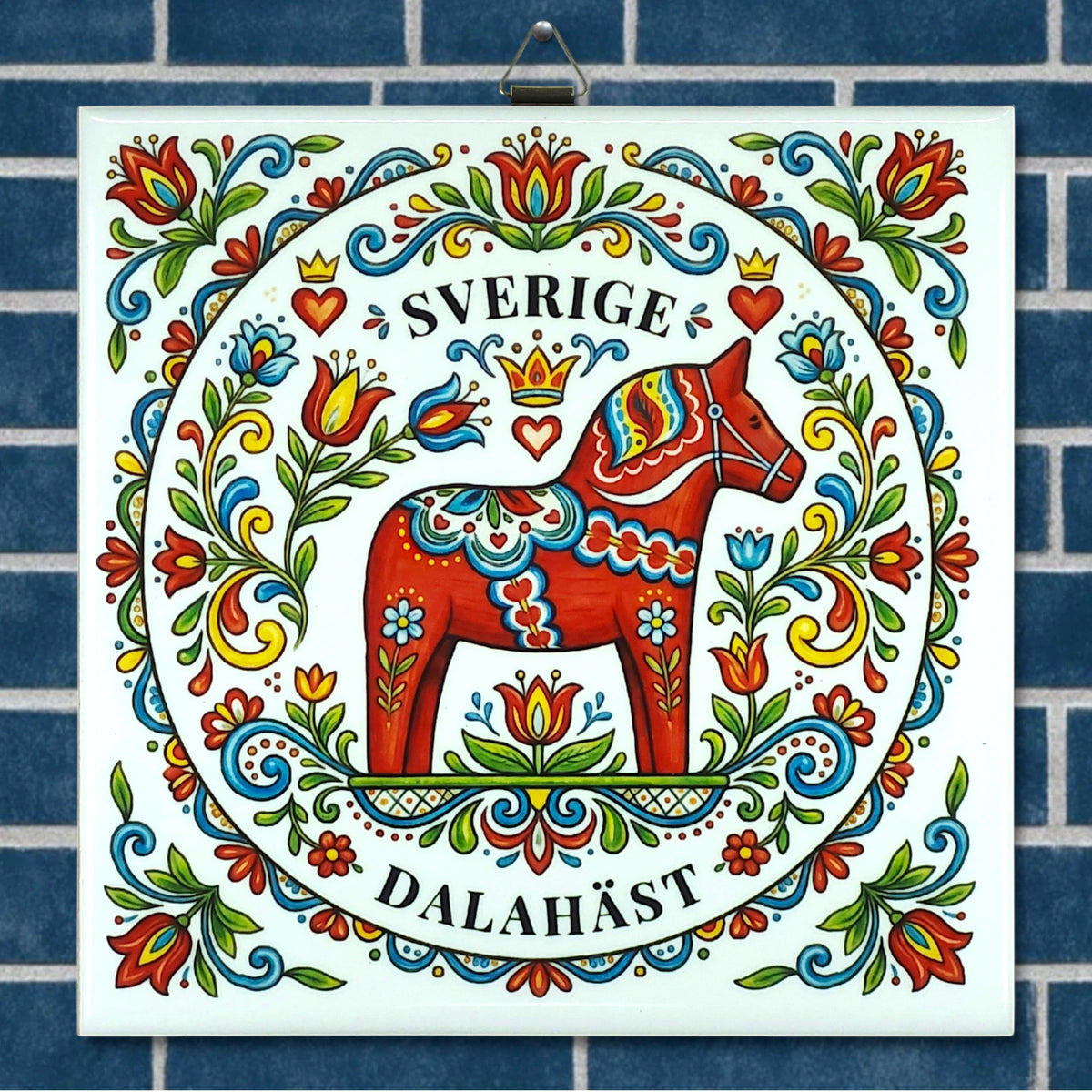 Ceramic tile with a red Swedish Dala horse, floral designs, and the words “Sverige” and “Dalahäst” on a blue-tiled background in Nordic folk art style.