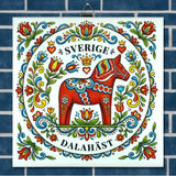 Ceramic tile with a red Swedish Dala horse, floral designs, and the words “Sverige” and “Dalahäst” on a blue-tiled background in Nordic folk art style.
