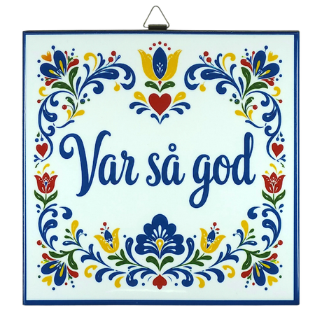 Cork-backed trivet with Norwegian and Swedish folk art patterns in blue, red, and yellow. The words “Var så god” are centered.