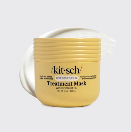 A yellow container of Kitsch Hair: Moisturizing Coconut Oil Deep Conditioning Treatment Mask 10 oz sits in front of a swoosh of white cream on a light gray background.