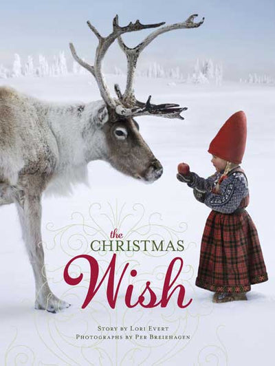 A young child in winter clothes offers an apple to a reindeer in a snowy scene, evoking holiday magic. The cover features the text “The Christmas Wish”—a book by Lori Evert and Per.
