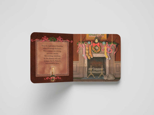 The Book: The Night Before Christmas – Classic Board Book Edition features Clement C. Moore's classic poem on the left page and a festive illustration of stockings above a fireplace on the right, capturing holiday magic.