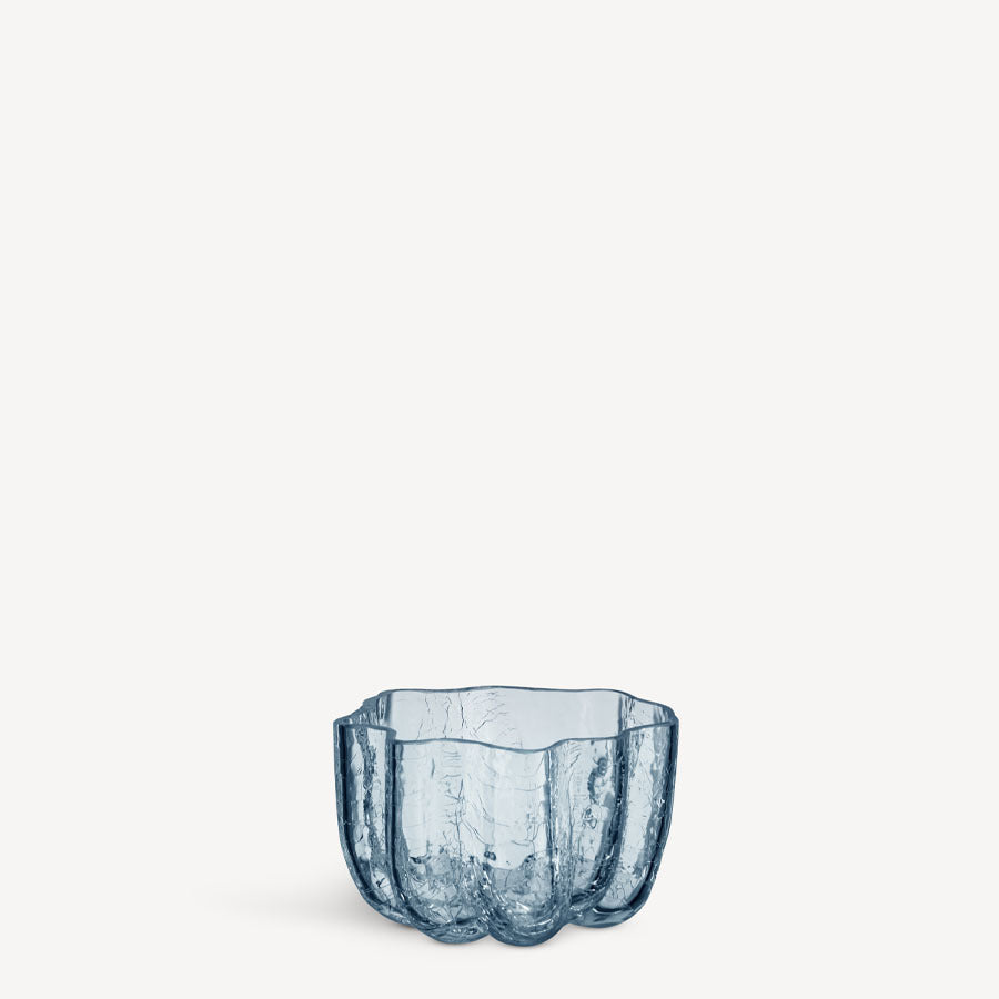 A blue, wavy-edged KostaBoda: Crackle Bowl Votive Circular with a textured surface is centered on a plain, light background.