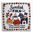 Ceramic tile featuring “Fika” and folk-art motifs: coffee, pastries, a Dala horse, flowers, and text reading “Coffee. Pastries. Friends. Scandinavian hospitality.”.