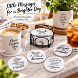 Coffee mugs and iced drinks on a wooden table in sunlight, with coasters displaying visible inspirational phrases.