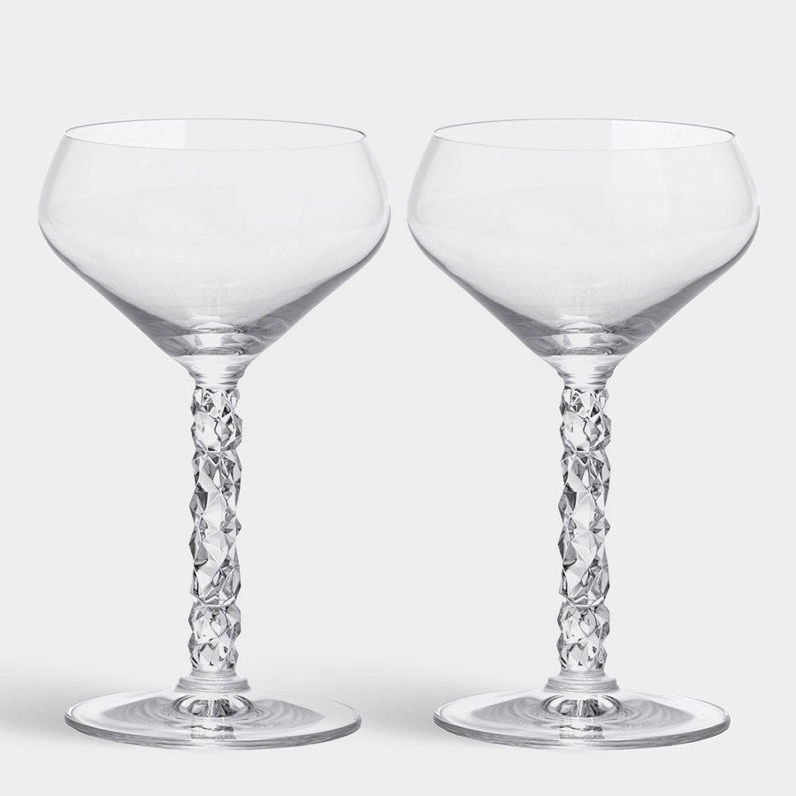 The two Orrefors: Carat Coupe 8.4oz wine glasses from a 2-pack feature intricately designed stems, standing elegantly against a plain backdrop, highlighting their crystal brilliance.